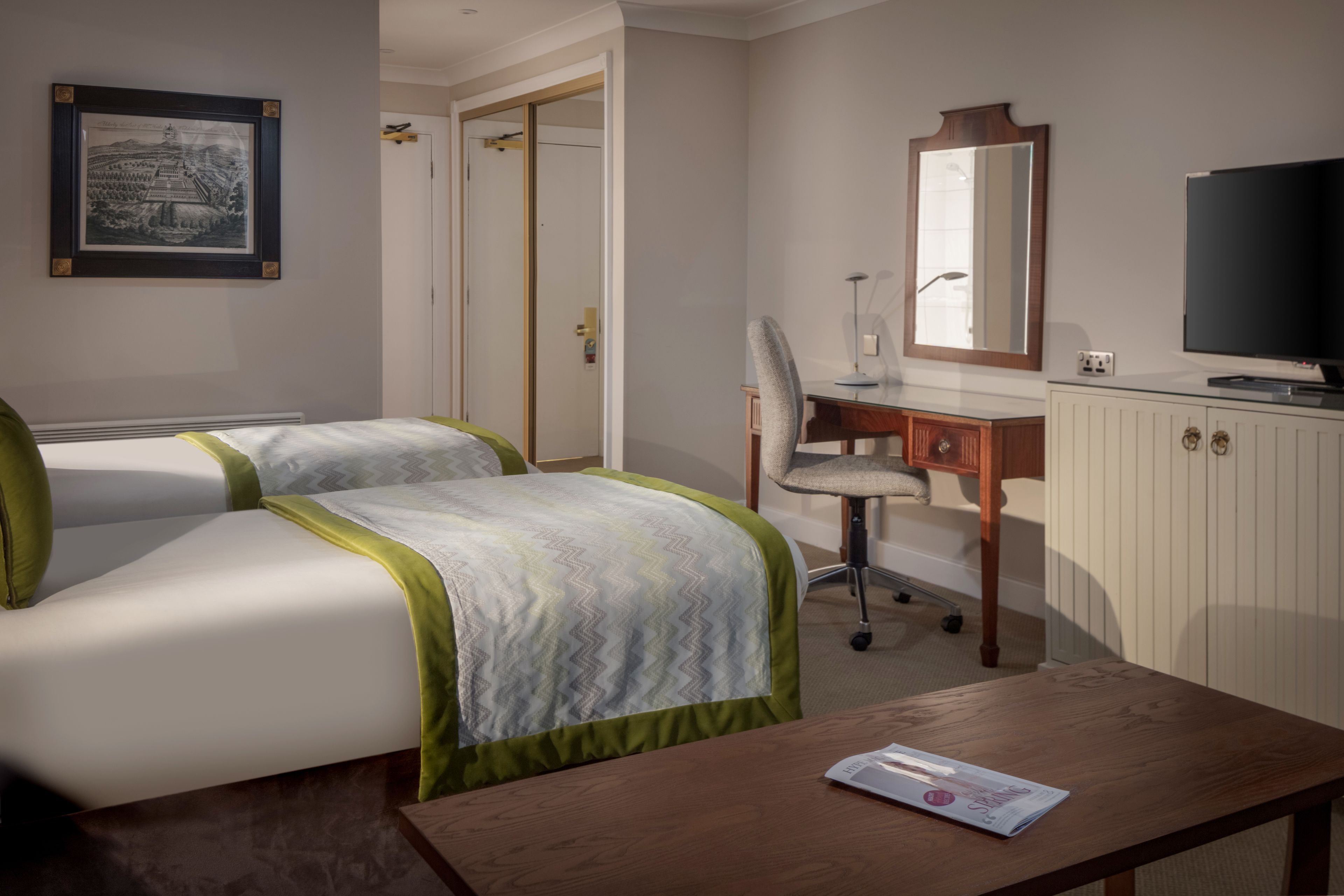 A hotel room with two beds, a desk, a chair, a television, and a framed picture on the wall.