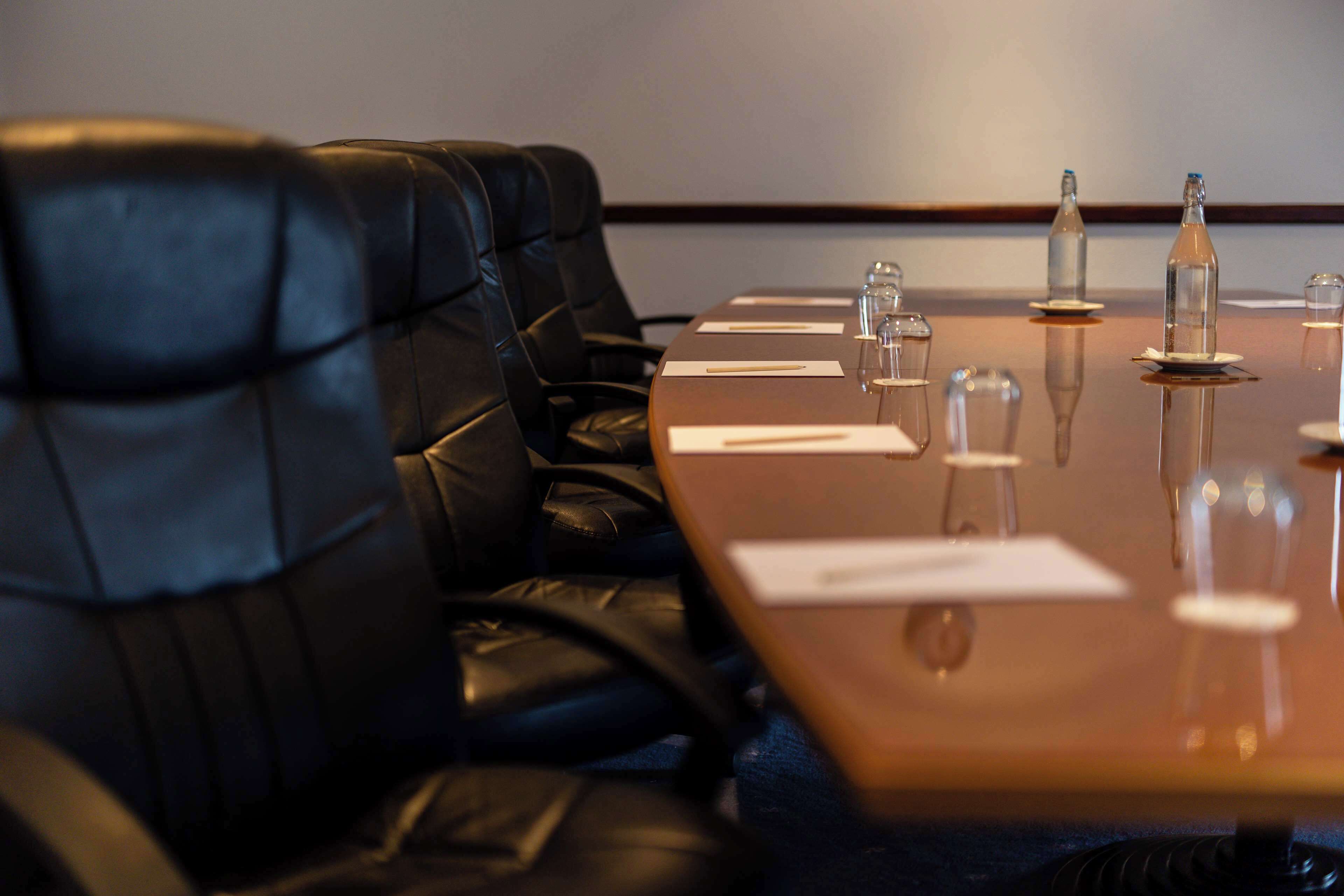 A conference room with a long table, black leather chairs, and clear glassware on the table.