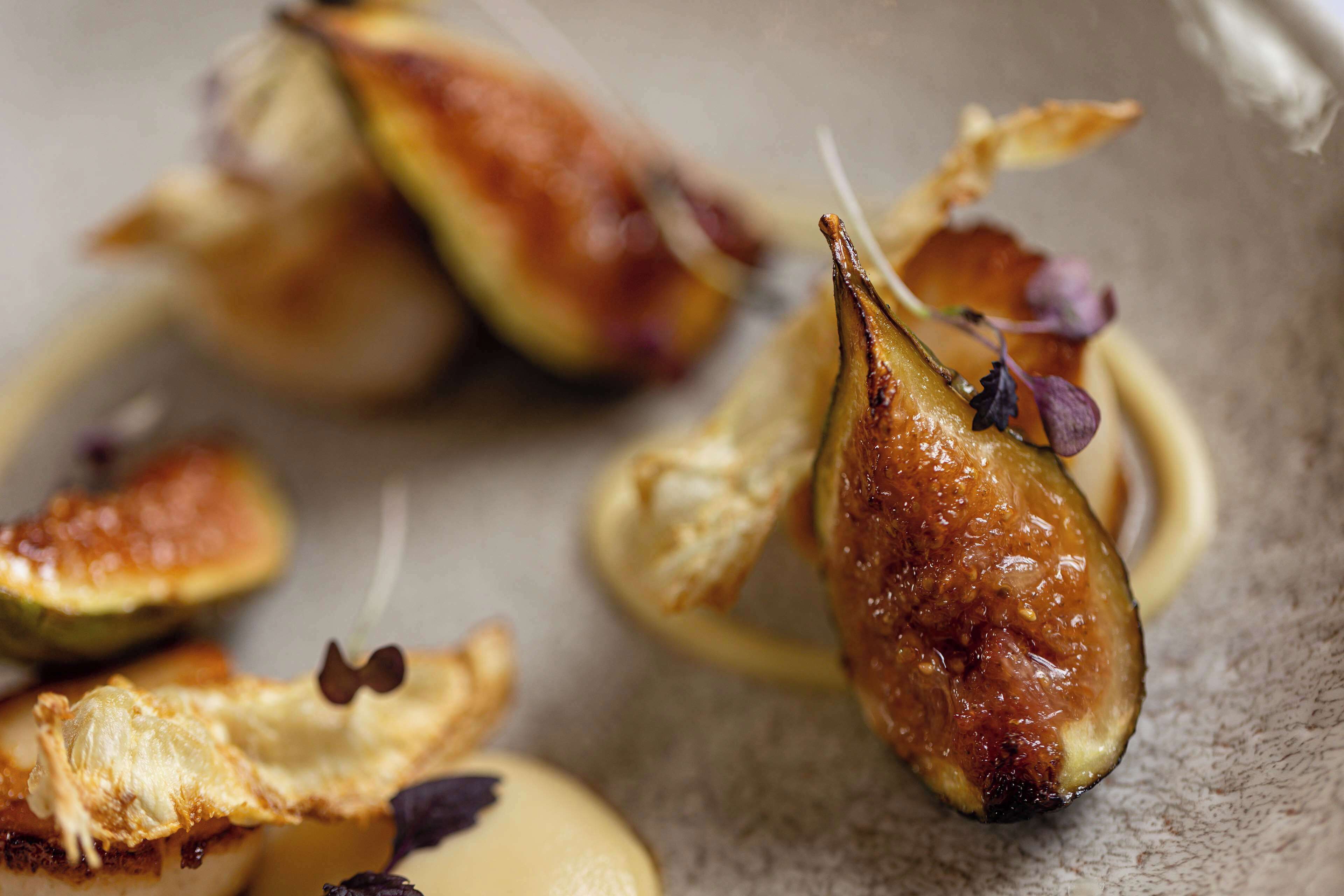 A close-up of a dish with roasted figs and a creamy sauce, garnished with edible flowers.
