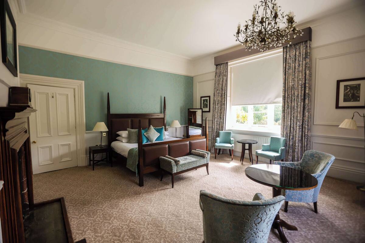 Une chambre d’hôtel dotée d’un grand lit, d’un coin salon avec un canapé et des fauteuils, d’un lustre et offrant une vue sur l’extérieur.