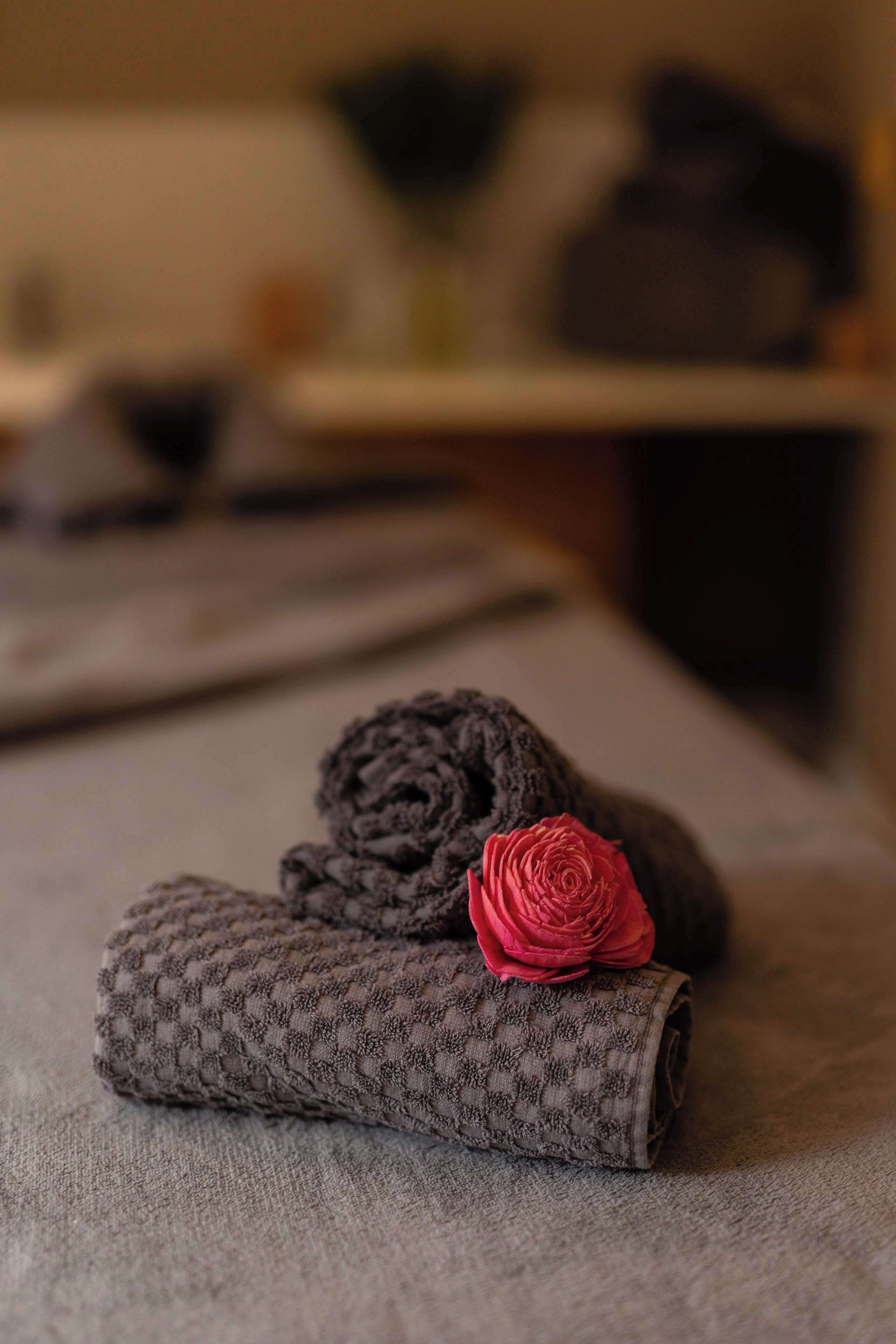 Un asciugamano grigio ordinatamente piegato con una rosa rossa su una superficie strutturata.