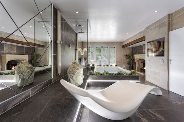 Un baño moderno con un espejo grande, una bañera blanca y una estatua de Buda de piedra.