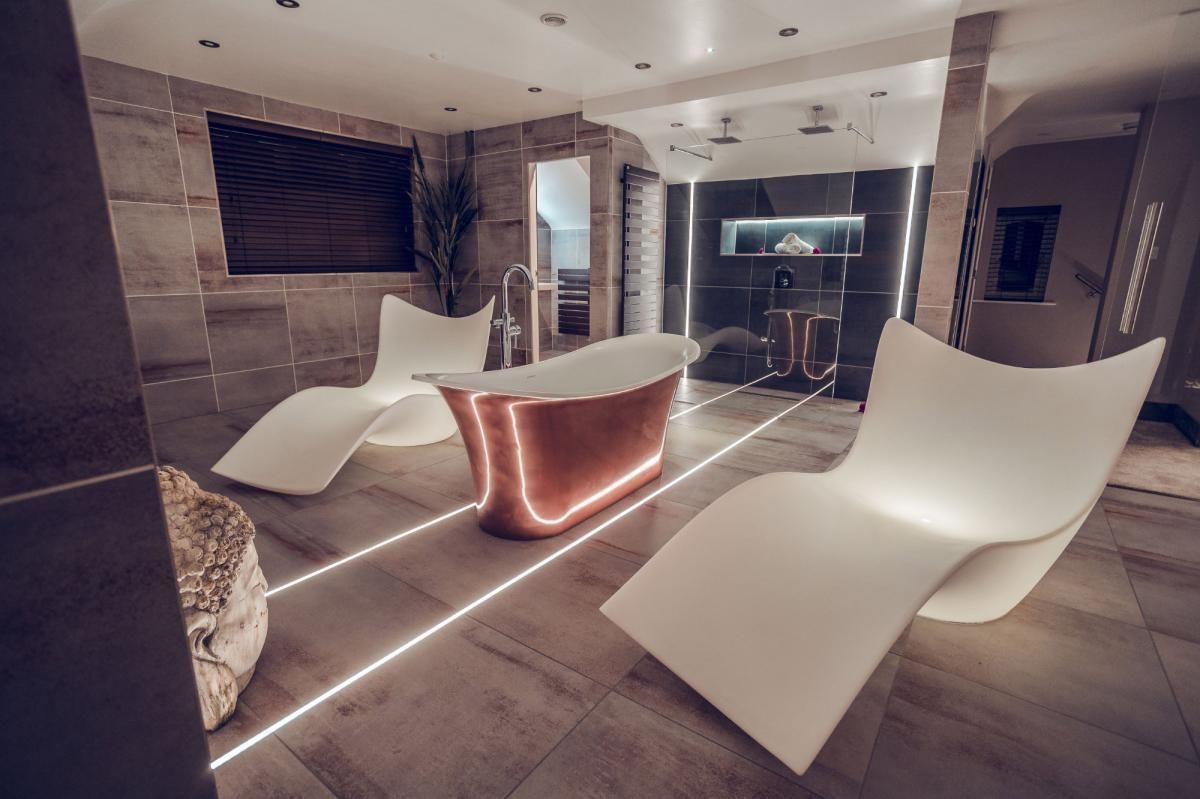 Une salle de bain moderne avec une baignoire sur pieds, deux chaises blanches et un grand miroir.
