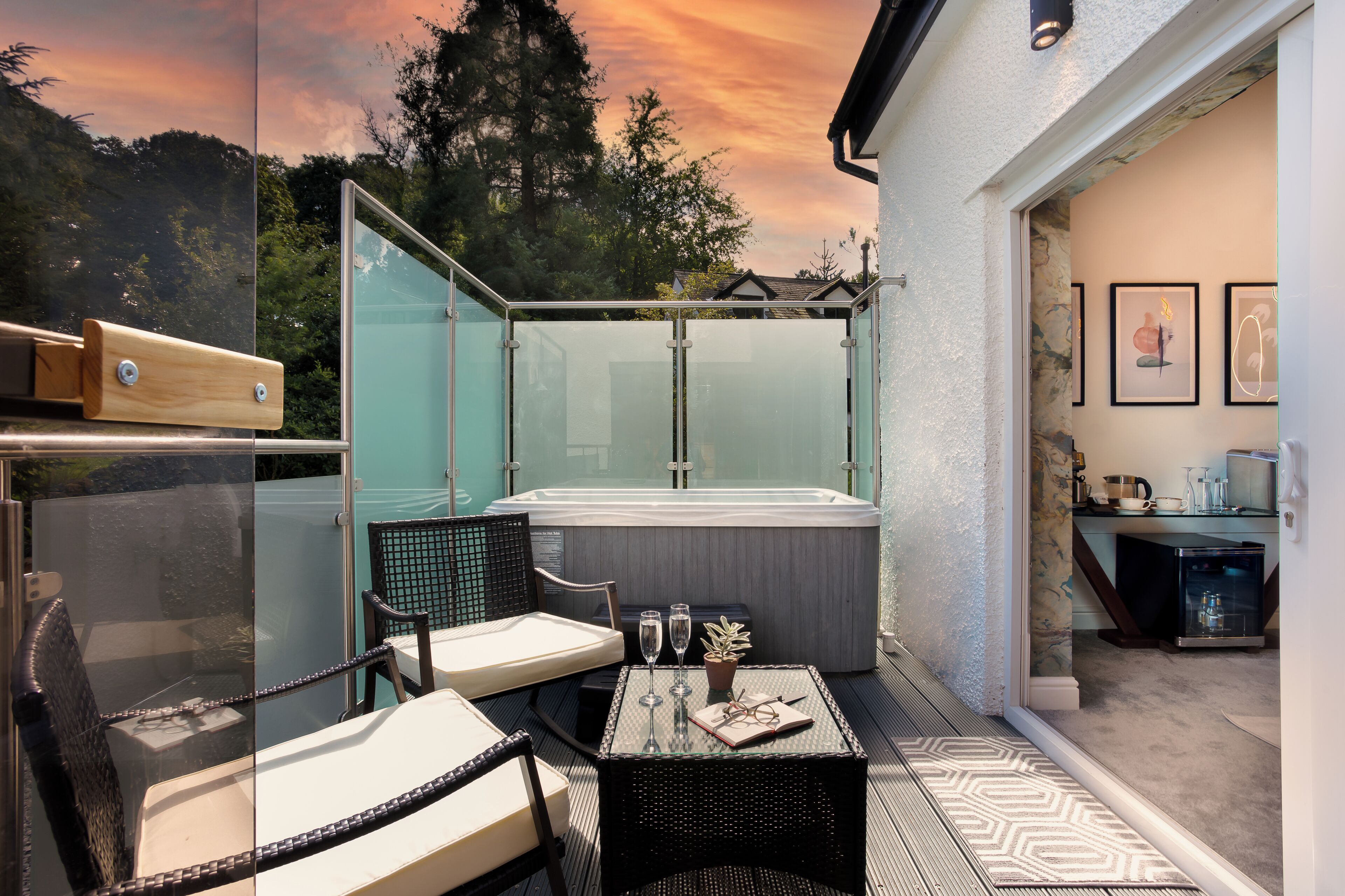 A balcony with a glass enclosure, a hot tub, outdoor seating, and a small table with glasses and a notebook.