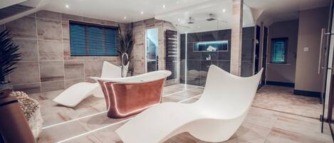 A modern bathroom with a large bathtub, a white lounge chair, and a glass shower enclosure.