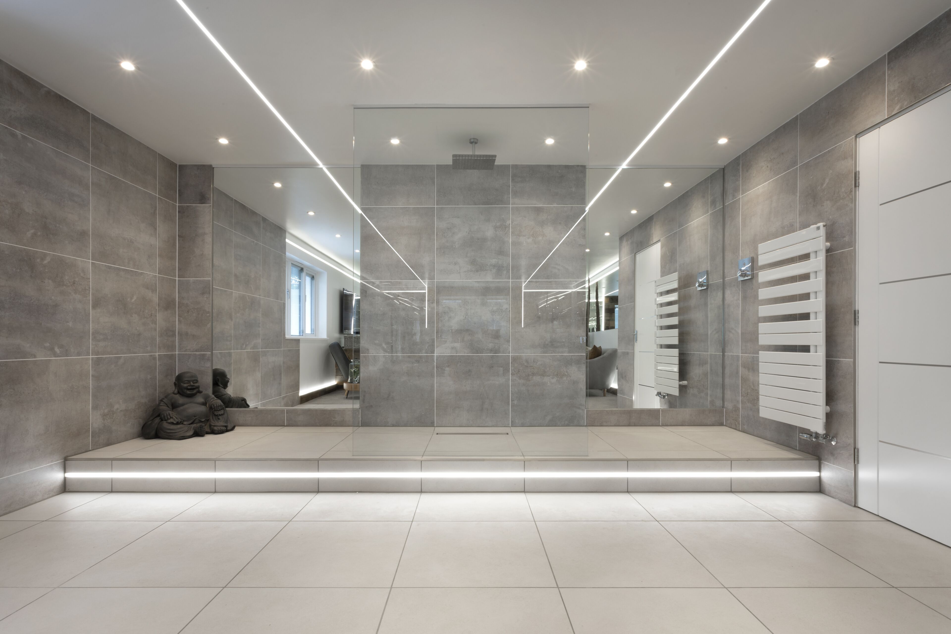 Un hall d’entrée moderne et spacieux, doté d’un design minimaliste, avec un espace salon central agrémenté d’une statue, d’un grand miroir et d’un radiateur.