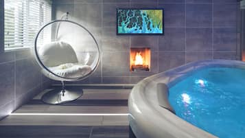 A modern bathroom with a hot tub, a hanging chair, and a fireplace.