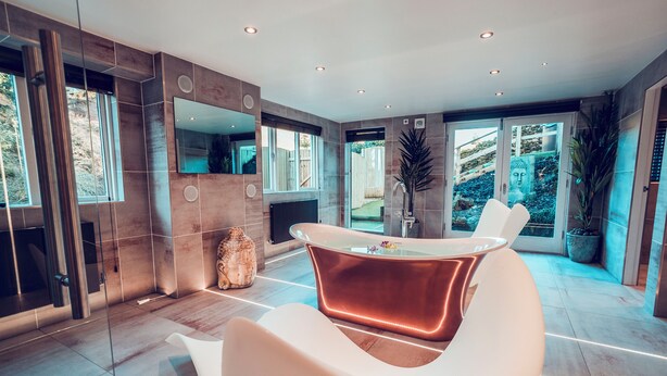 Un baño moderno con bañera de hidromasaje con mampara de vidrio, un espejo grande y una zona de estar.