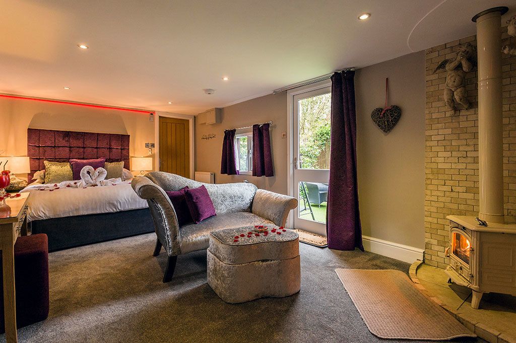 A modern bedroom with a bed, a sofa, a fireplace, and a large window.