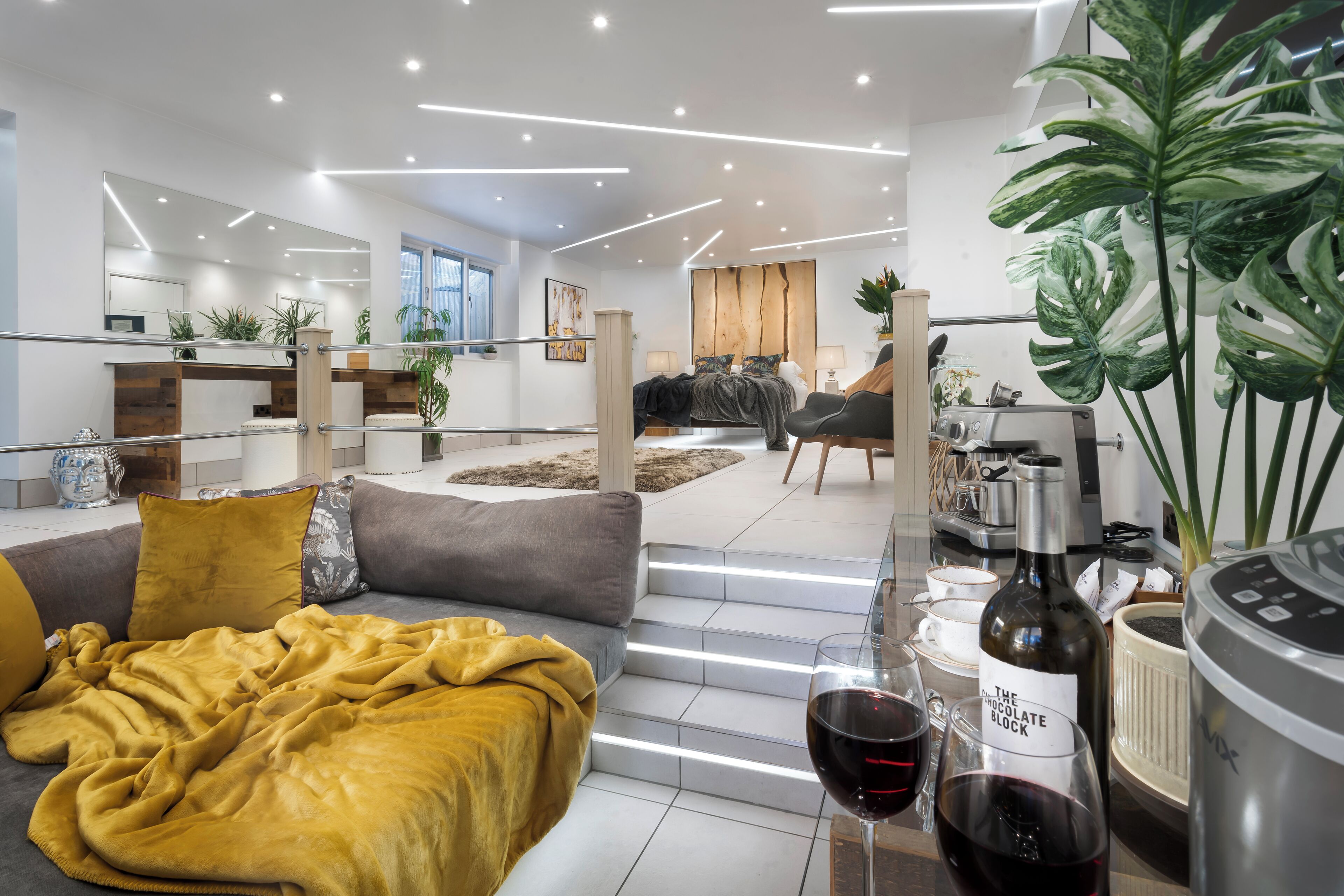 Ein modernes Wohnzimmer mit einer Couch, einem Couchtisch mit Weingläsern und einer Küche im Hintergrund.