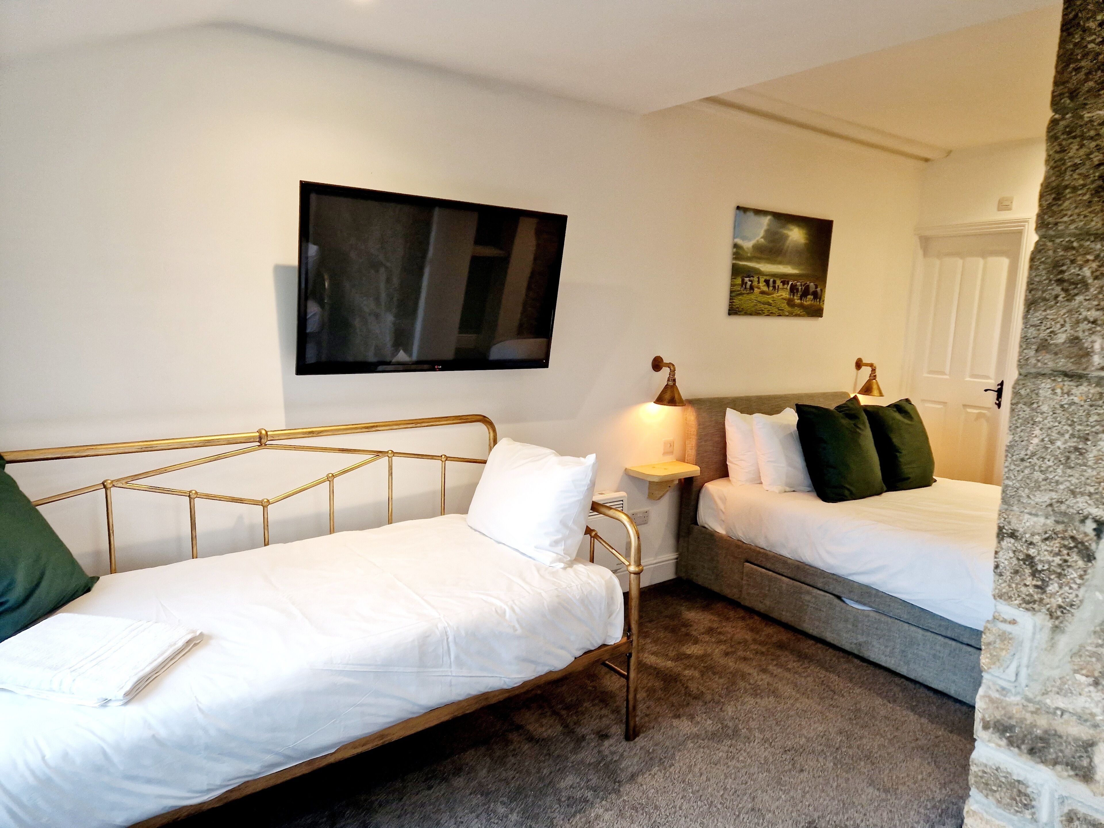 A bedroom with two single beds, a television, a wall-mounted lamp, and a picture.