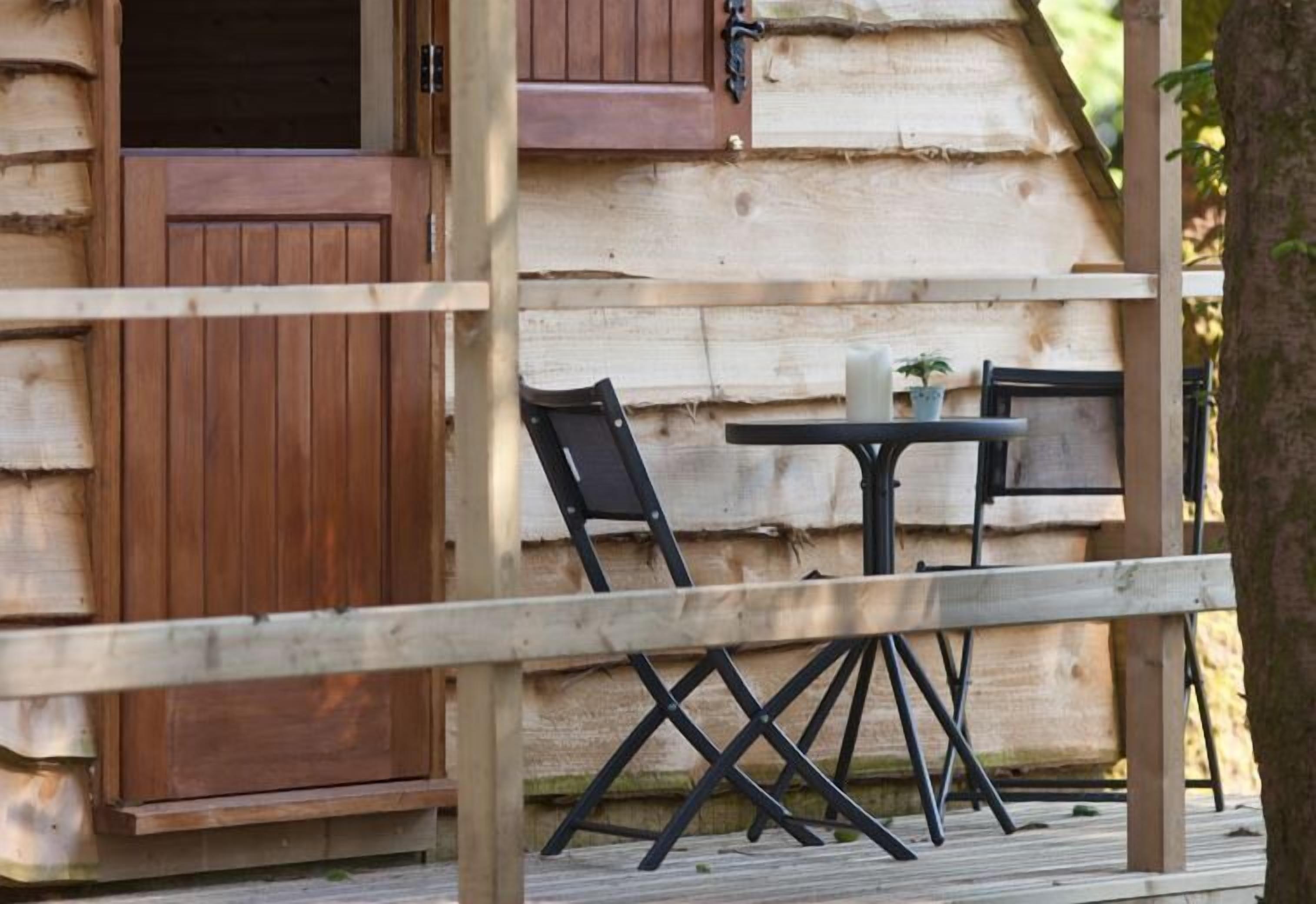 A wooden cabin with a porch, a table, and two chairs.