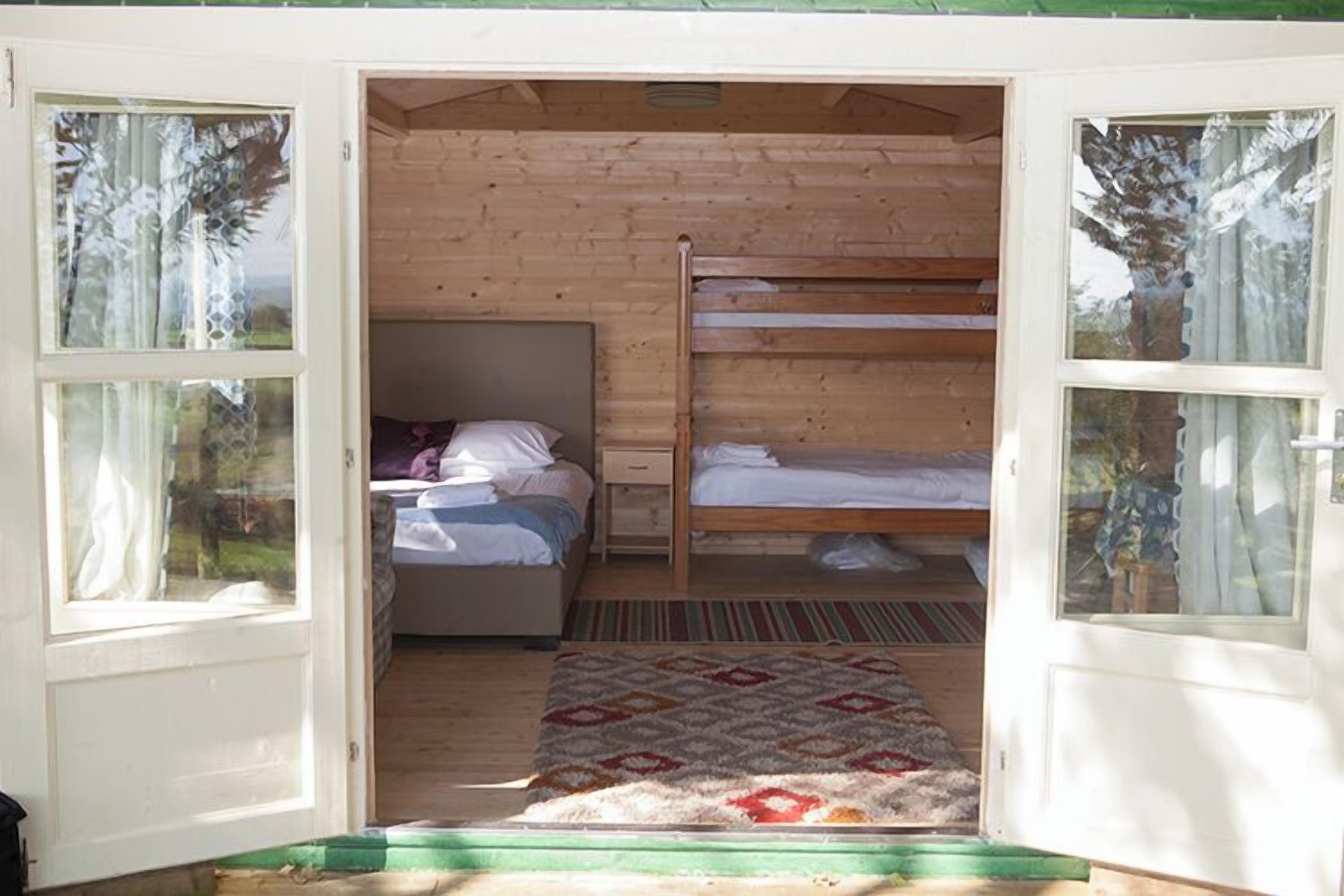 A wooden cabin with a bunk bed, a single bed, and a window with curtains.