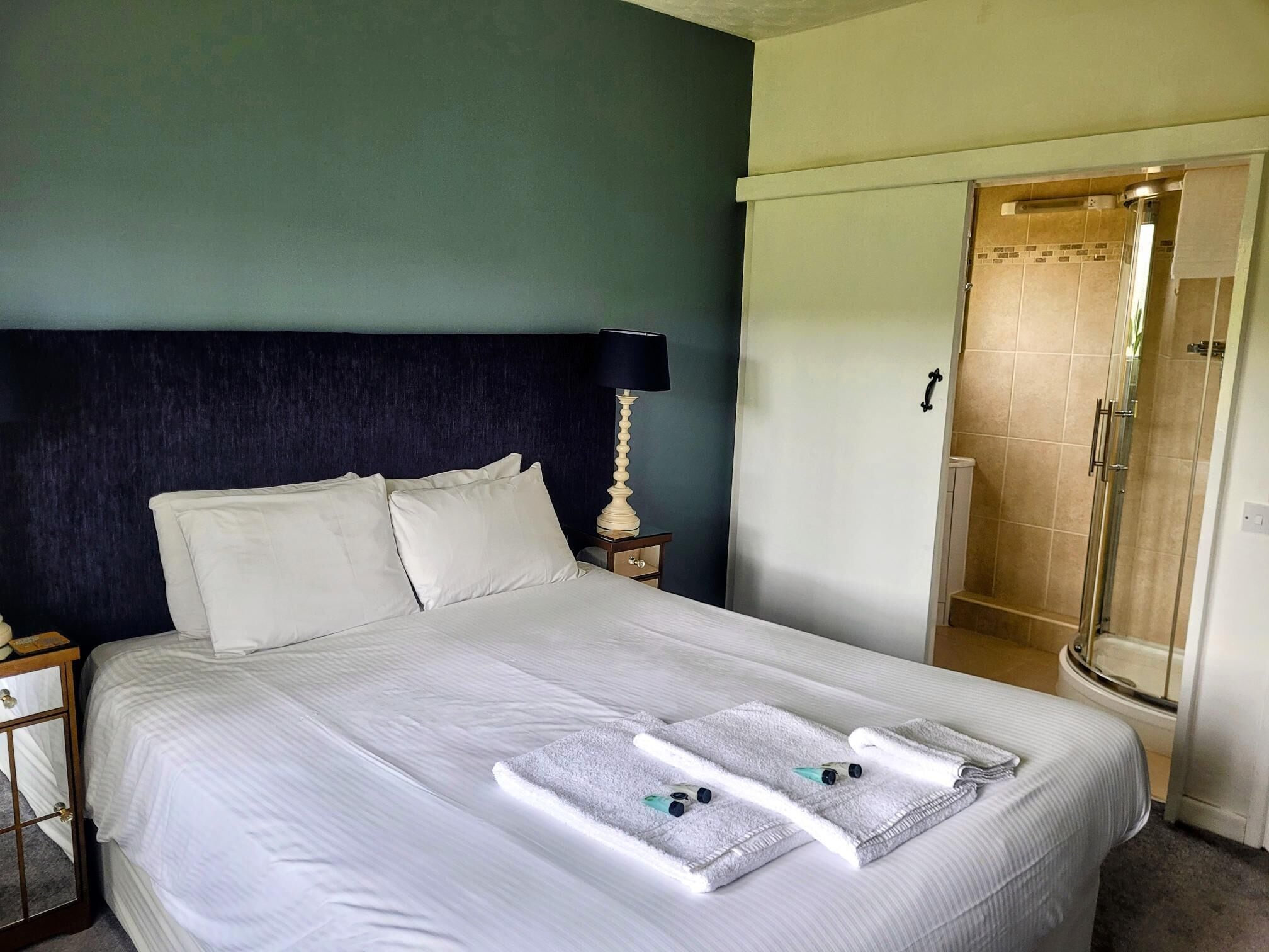 A neatly made bed with white linens and two towels folded on top.