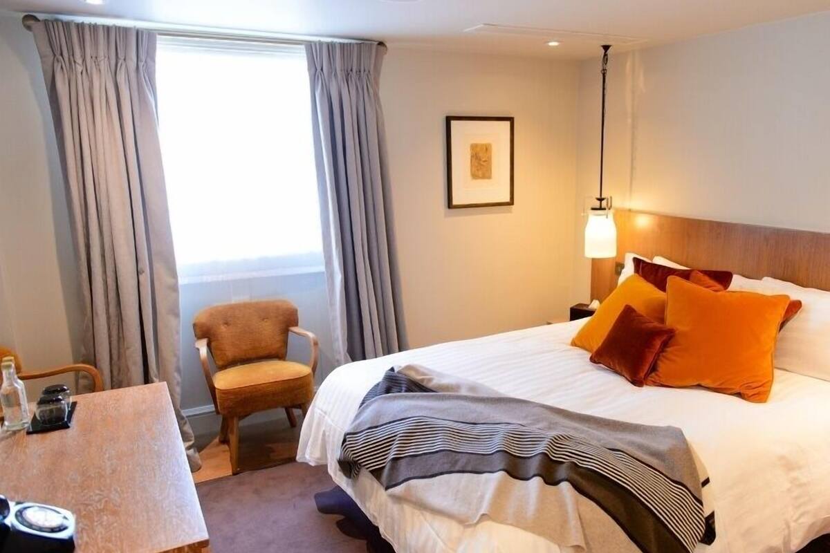 A hotel room with a bed, a chair, a desk, and a window with curtains.