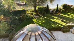 Una estructura de cúpula transparente con vistas a un jardín y una masa de agua al fondo.