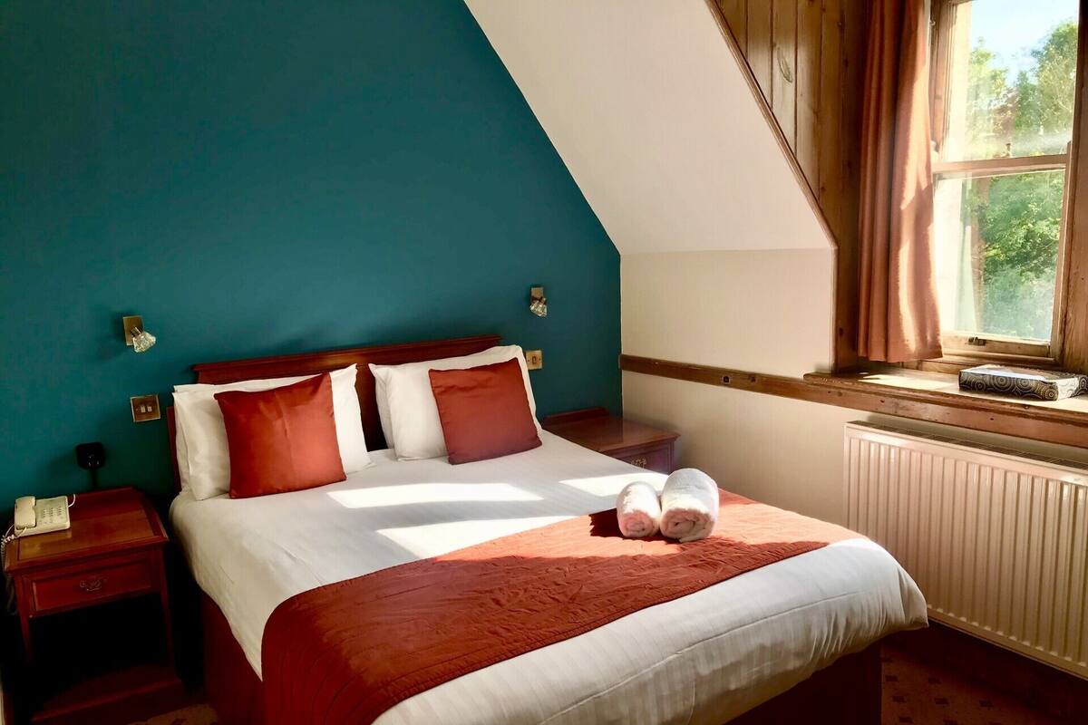 A bedroom with a bed, two bedside tables, a window with curtains, and a radiator.