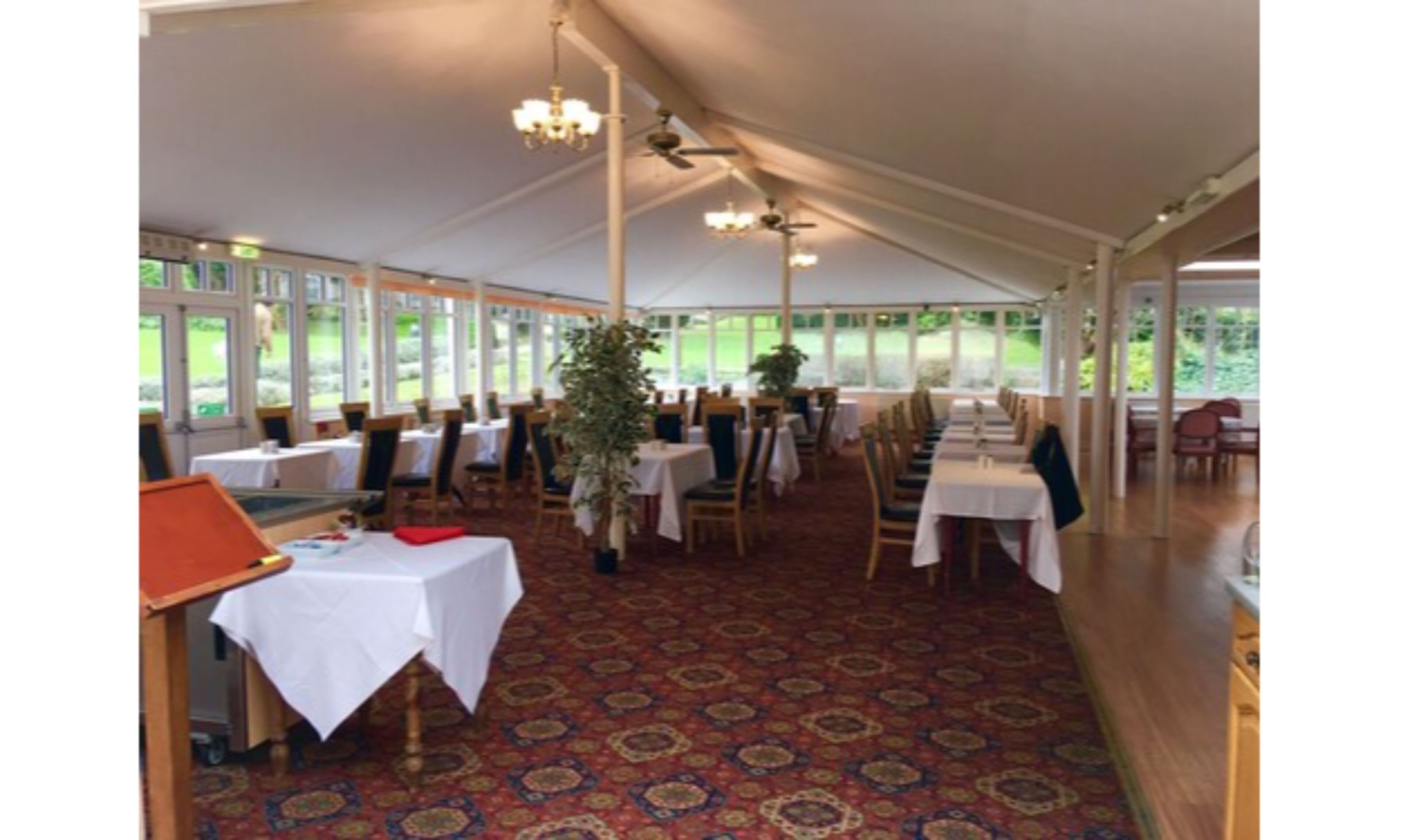 A tented dining area with tables and chairs, large windows, and ceiling fans.