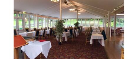 A tented dining area with tables and chairs, large windows, and ceiling fans.