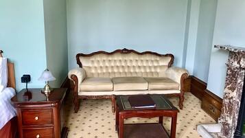 A room with a tufted sofa, a wooden nightstand with drawers, a small table, and a decorative column.