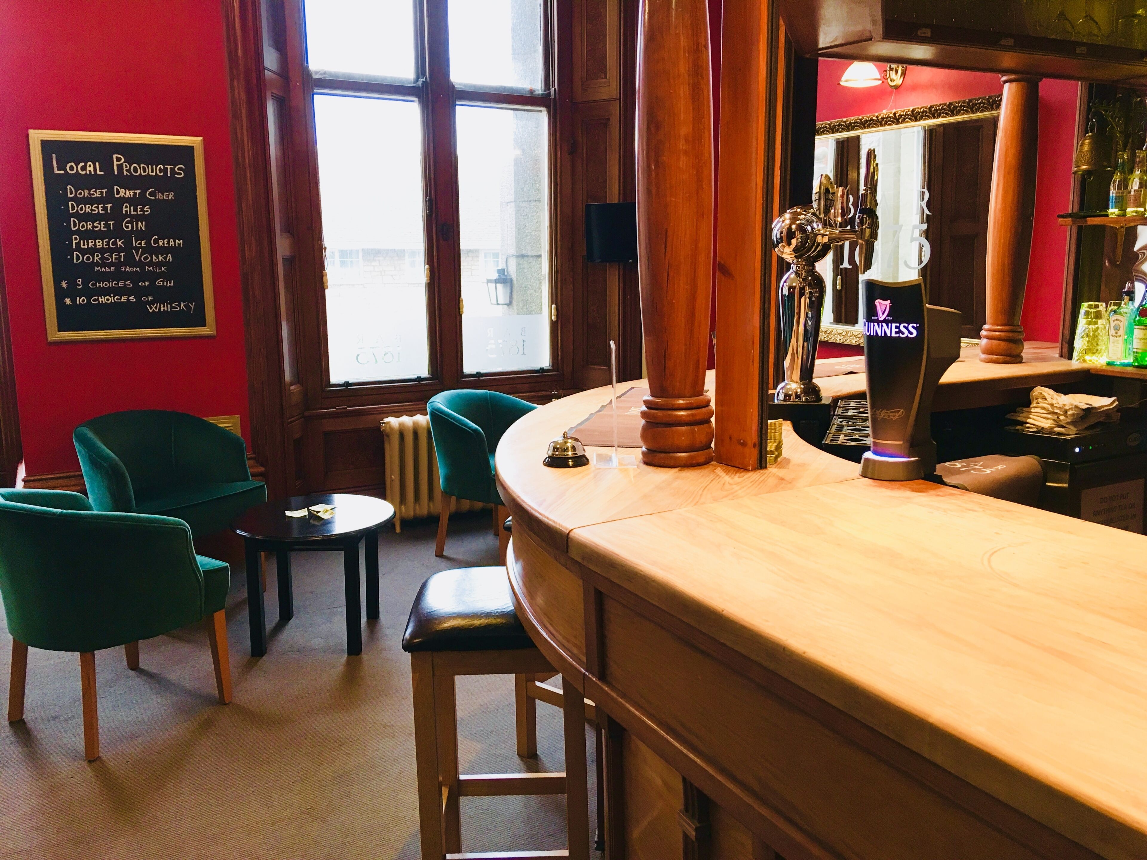 A bar area with a wooden counter, green chairs, a sign listing local products, and a Guinness beer tap.