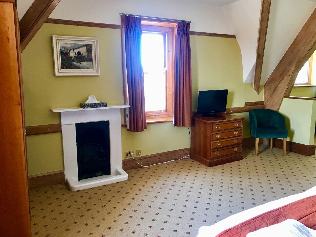 A room with a fireplace, a television, a wooden dresser, a teal chair, and a window with curtains.