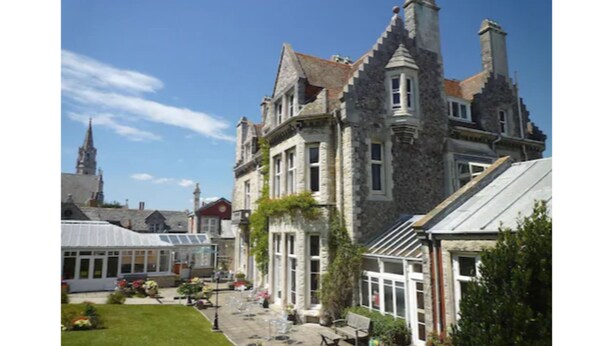 A historic stone building with a large garden and a church in the background. - Purbeck House Hotel (Swanage)
