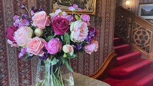 A vase of flowers on a marble table in a room with patterned wallpaper and a staircase. - Purbeck House Hotel (Swanage)