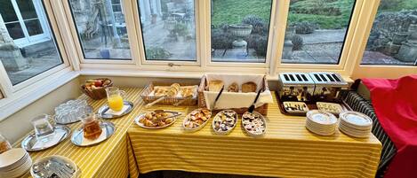 A breakfast buffet setup with various food items and utensils on a table, viewed through large windows.