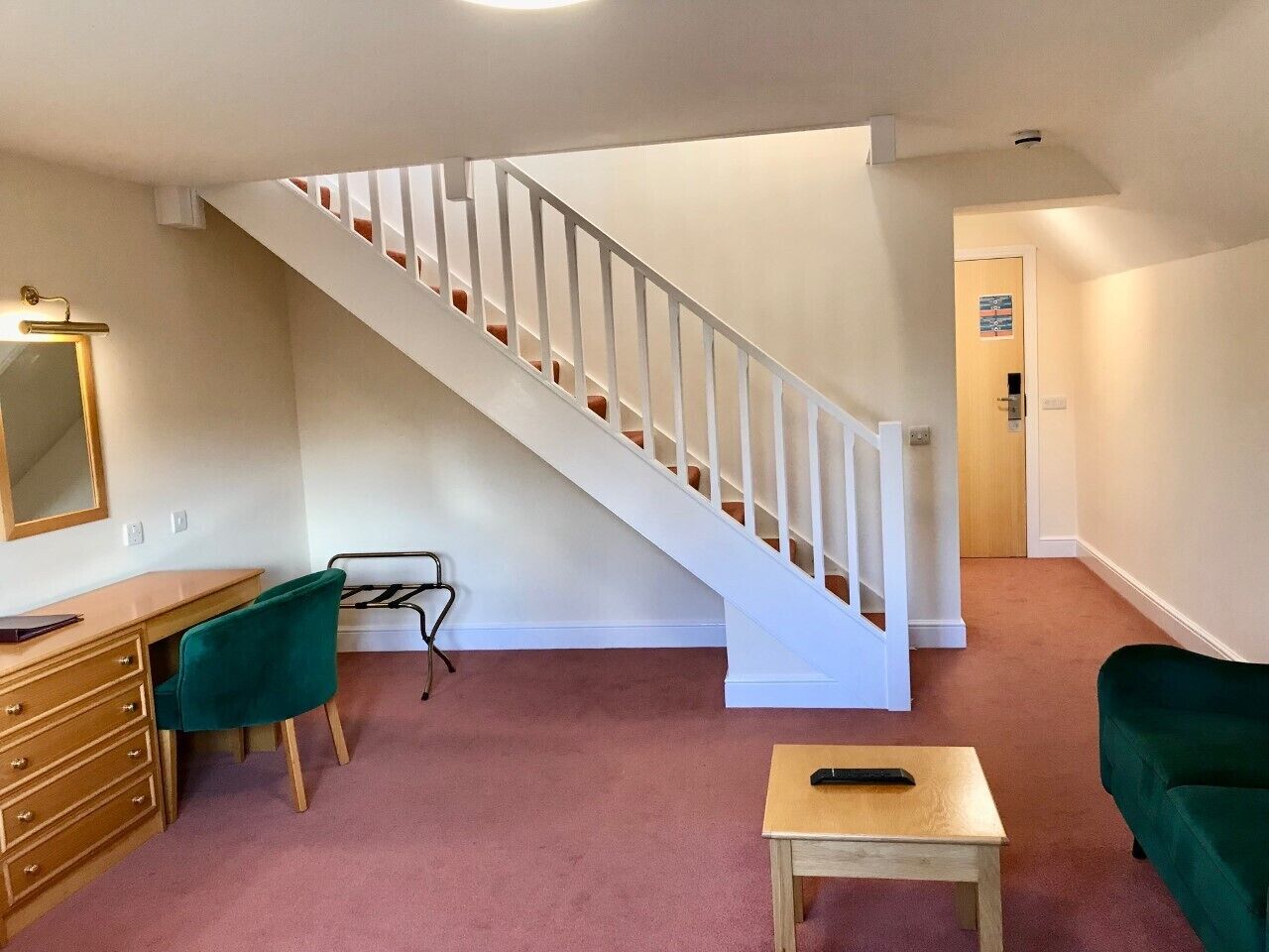 A room with a staircase, a desk with a chair, a small table, and a green sofa.
