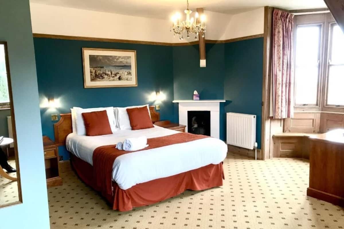 A bedroom with a large bed, a fireplace, a chandelier, and a window with curtains.