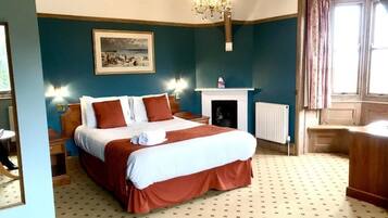 Quarto com uma cama grande, lareira, candelabro e janela com cortinas.