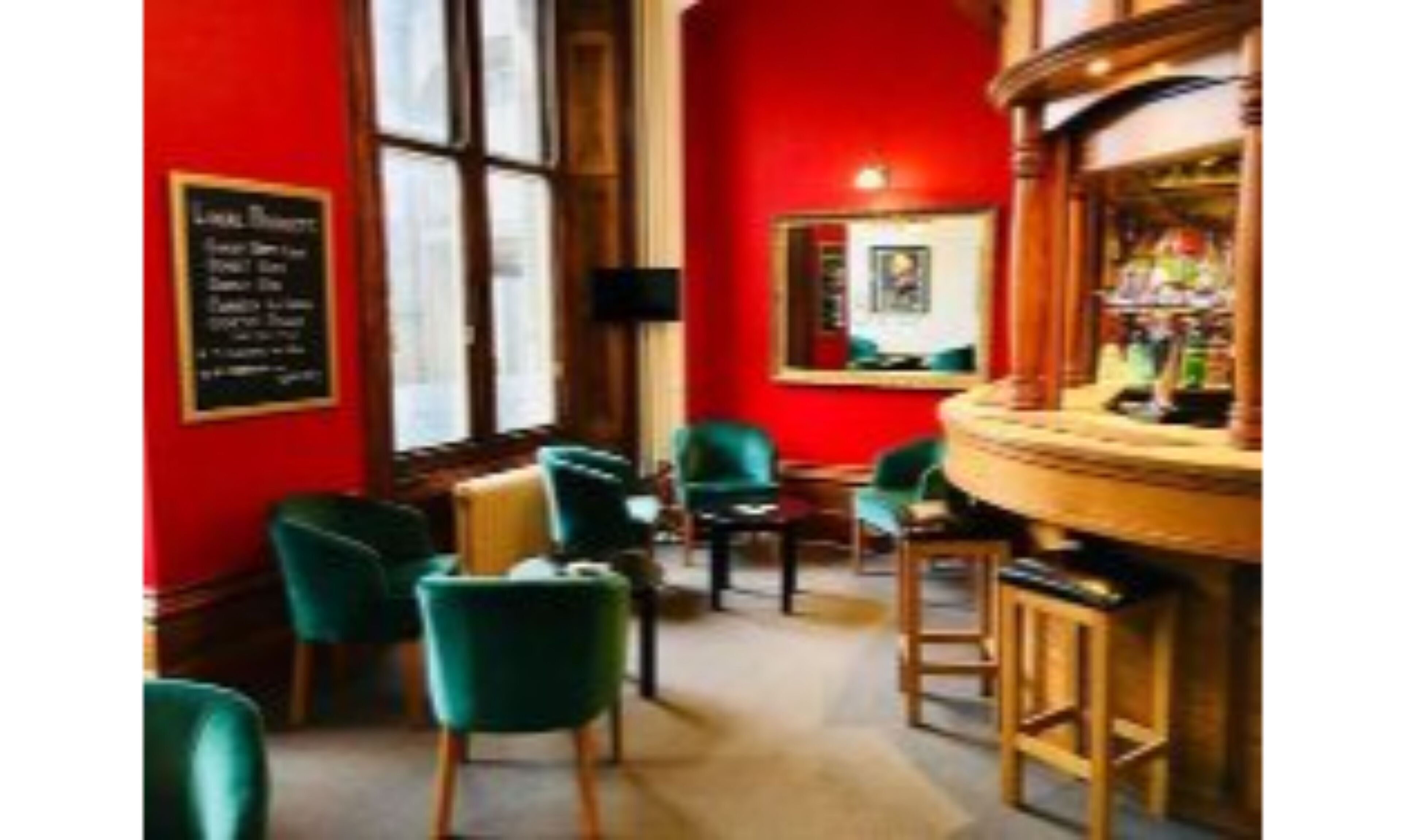 A bar area with green chairs, wooden bar stools, and red walls.