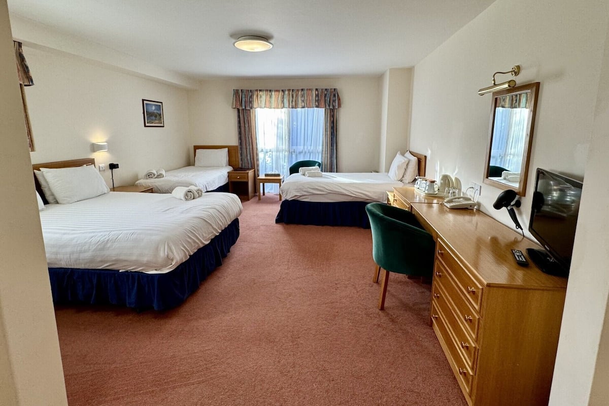 A hotel room with two beds, a desk with a chair, a television, and a window with curtains.
