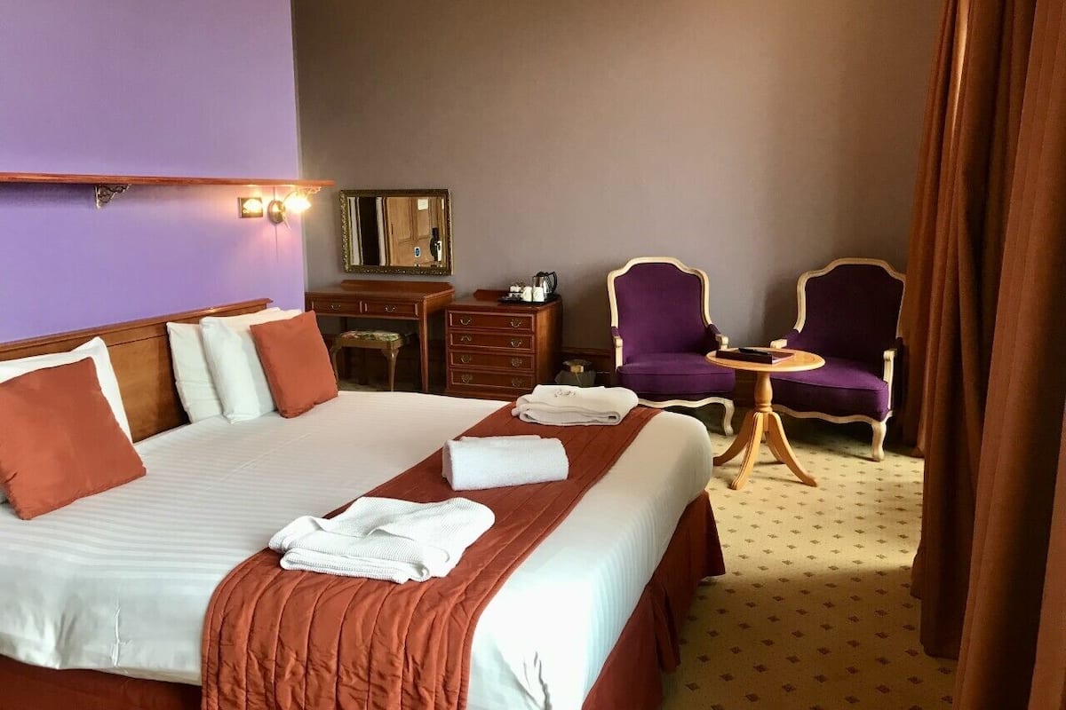 A hotel room with a large bed, two armchairs, a small round table, and a dresser.