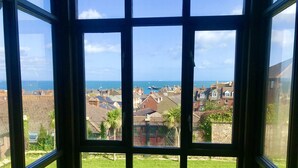 A view through a window with a clear sky, a grassy yard, and a distant town with buildings and the sea. - Purbeck House Hotel (Swanage)