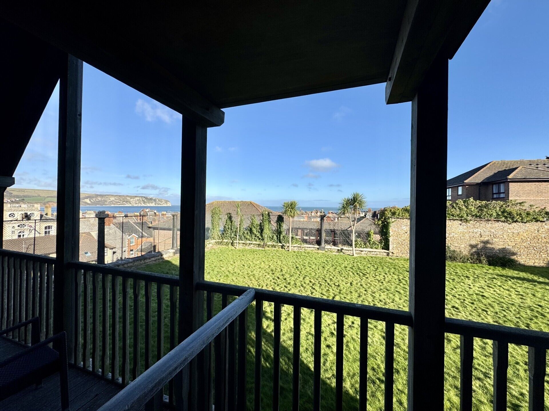 A balcony with a view of a grassy area, a stone wall, and buildings in the distance.