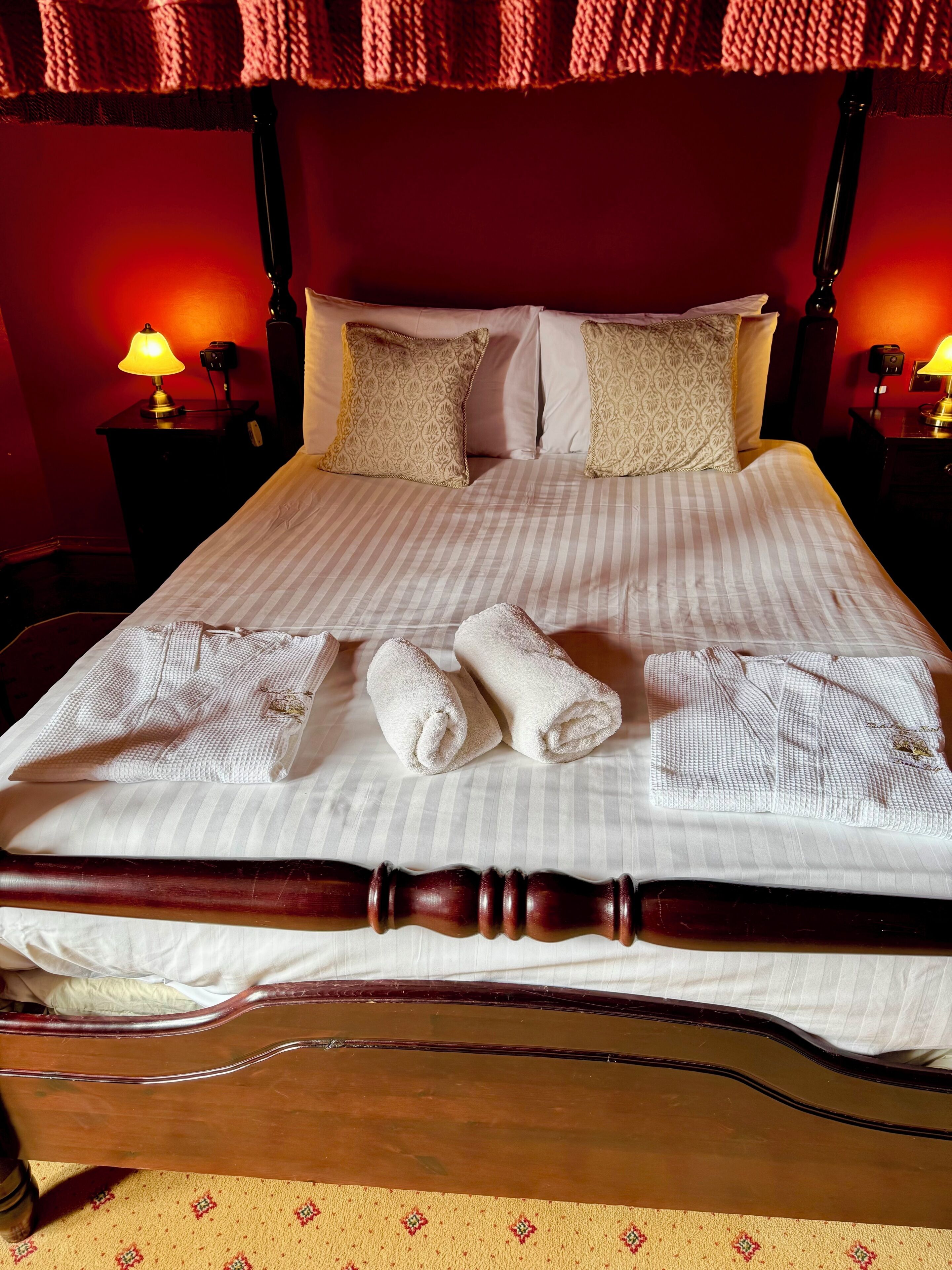 A neatly made bed with striped bedding, two pillows with a floral pattern, and two rolled towels.