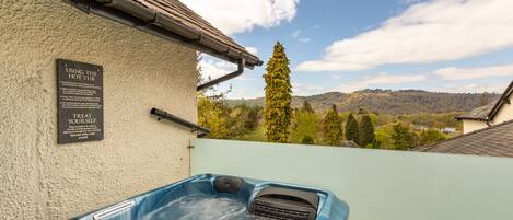 Un bain à remous avec un panneau indiquant les règles d’utilisation, et en arrière-plan, une vue sur des arbres et des collines.