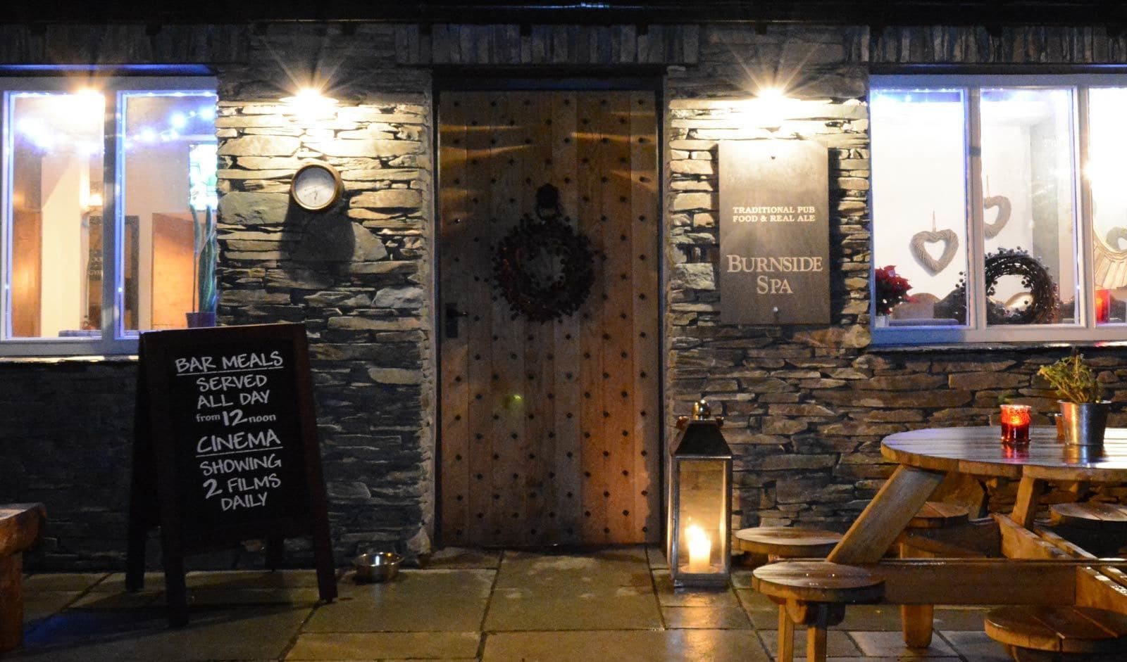A traditional pub with stone walls, a wooden door, and a sign indicating bar meals, cinema, and spa services.