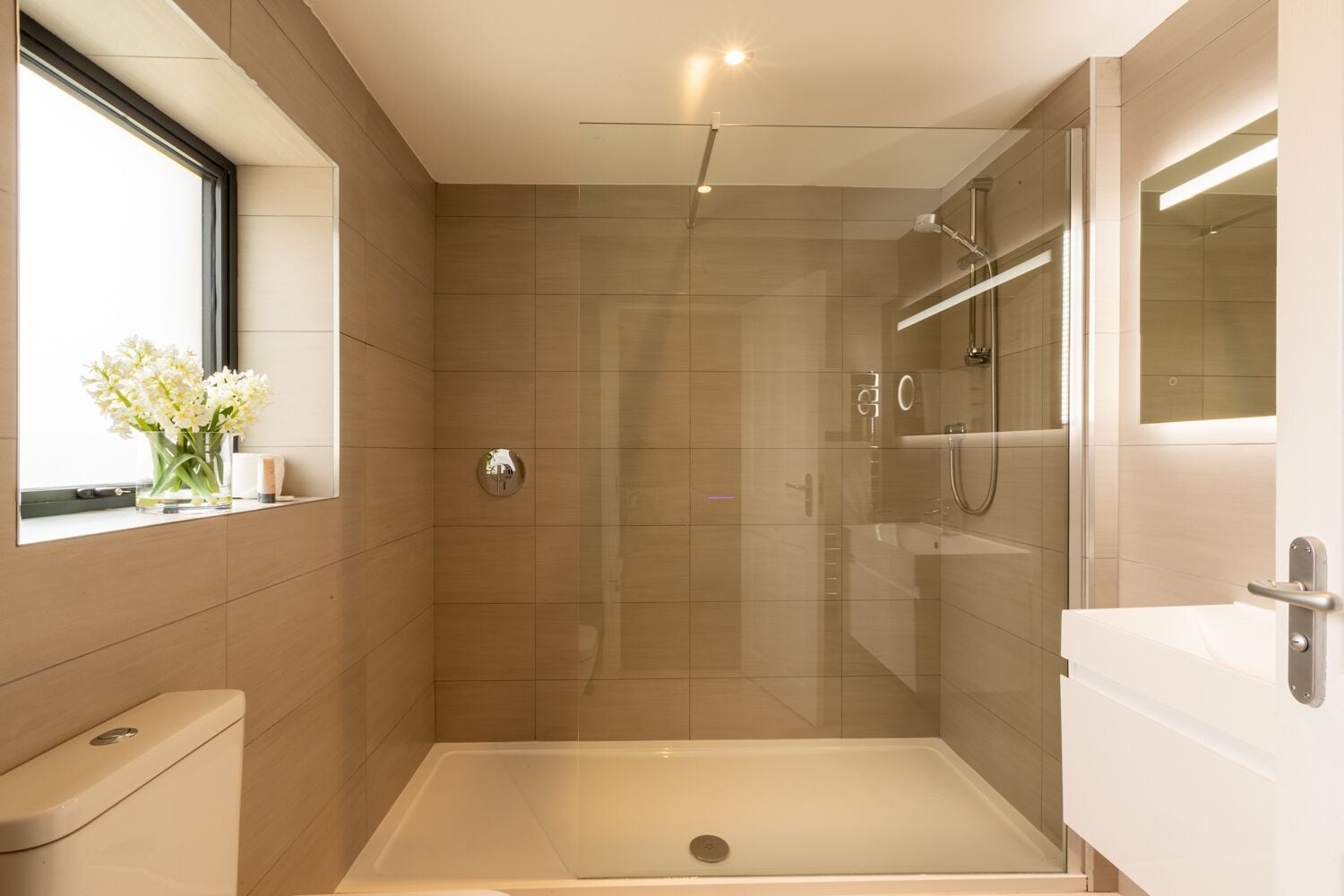 A modern bathroom with a glass-enclosed shower, a toilet, and a sink.