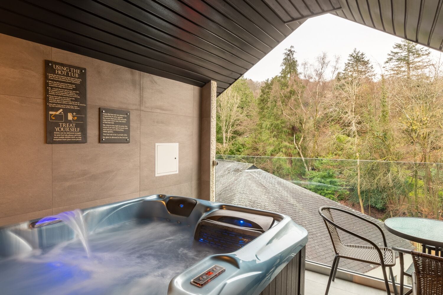 A hot tub with a control panel, two informational signs, and a view of a forested area.