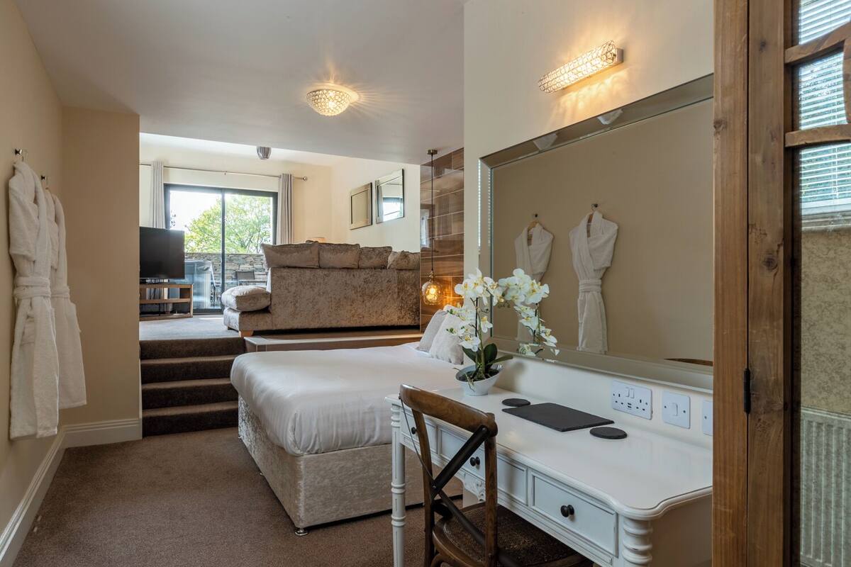 A well-lit bedroom with a large bed, a vanity with a mirror, and a sofa in the background.