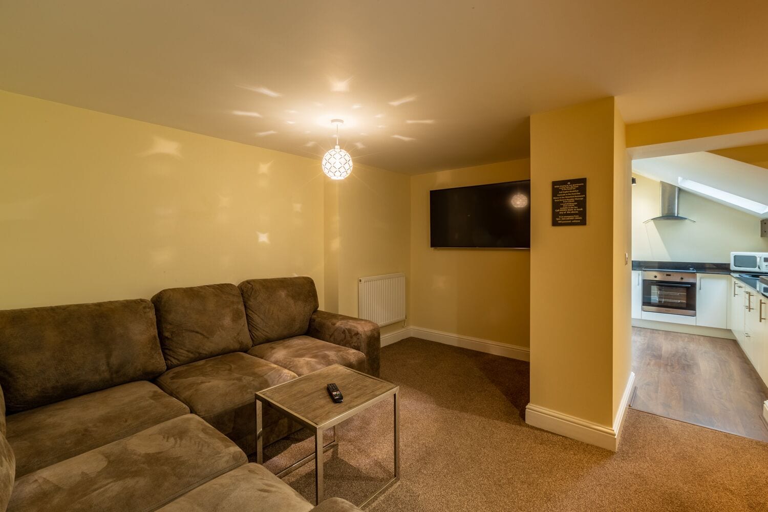 A living room with a brown sectional sofa, a glass coffee table, and a TV mounted on the wall.