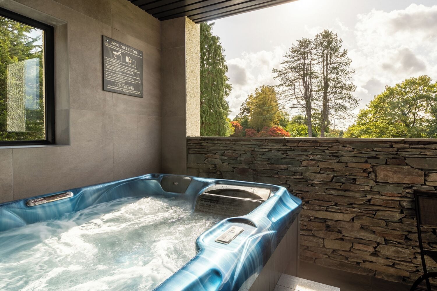 Ein Whirlpool mit einer Steinwand im Hintergrund und einem Fenster mit Blick auf Bäume.
