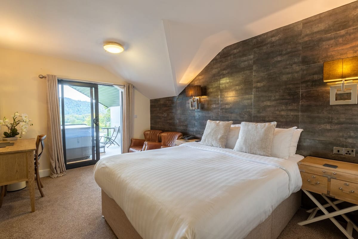 A modern hotel room with a large bed, a desk, and a balcony with a view.