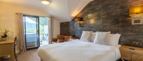 A modern hotel room with a large bed, a desk, and a balcony with a view.