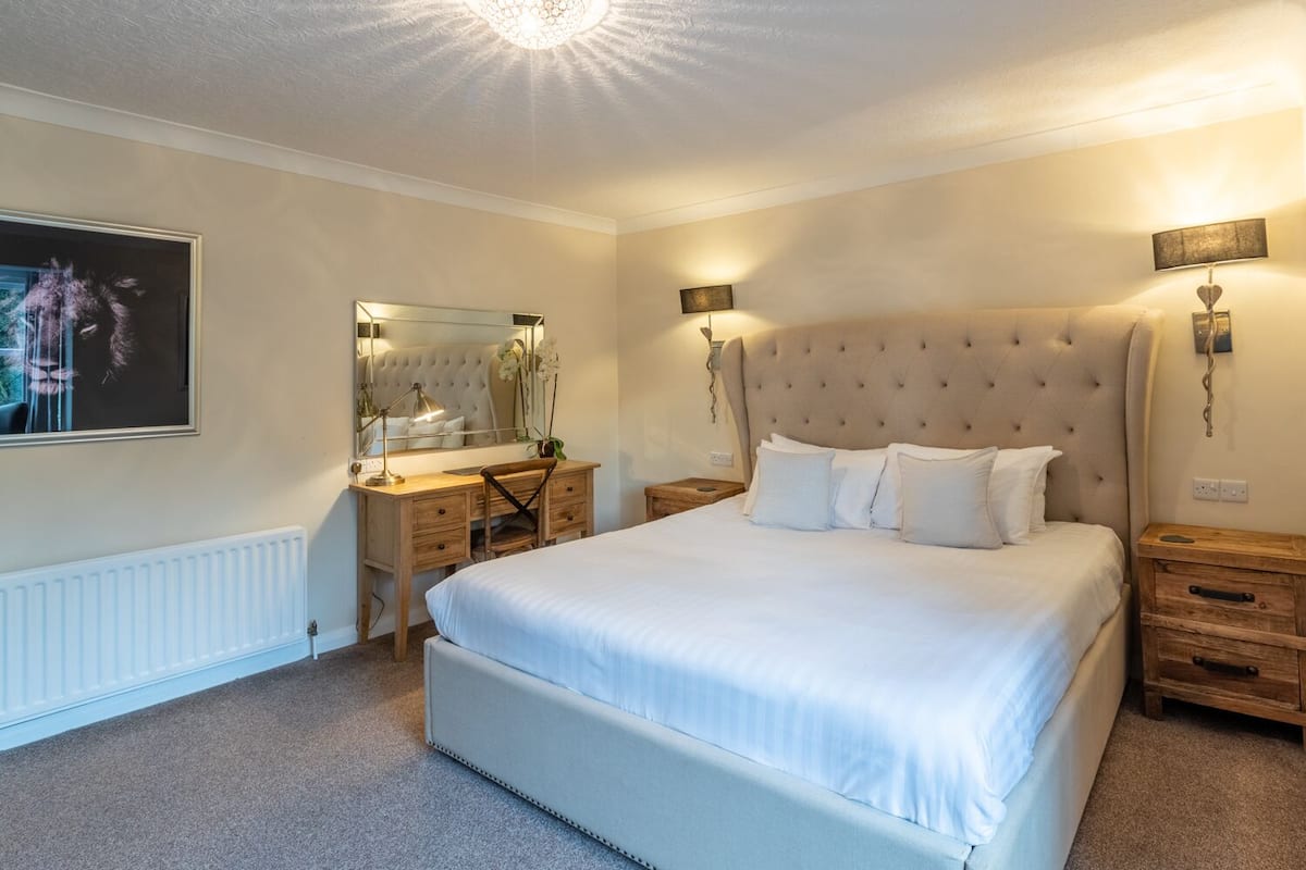 A bedroom with a large bed, a wooden dresser, a mirror, and two bedside tables with lamps.