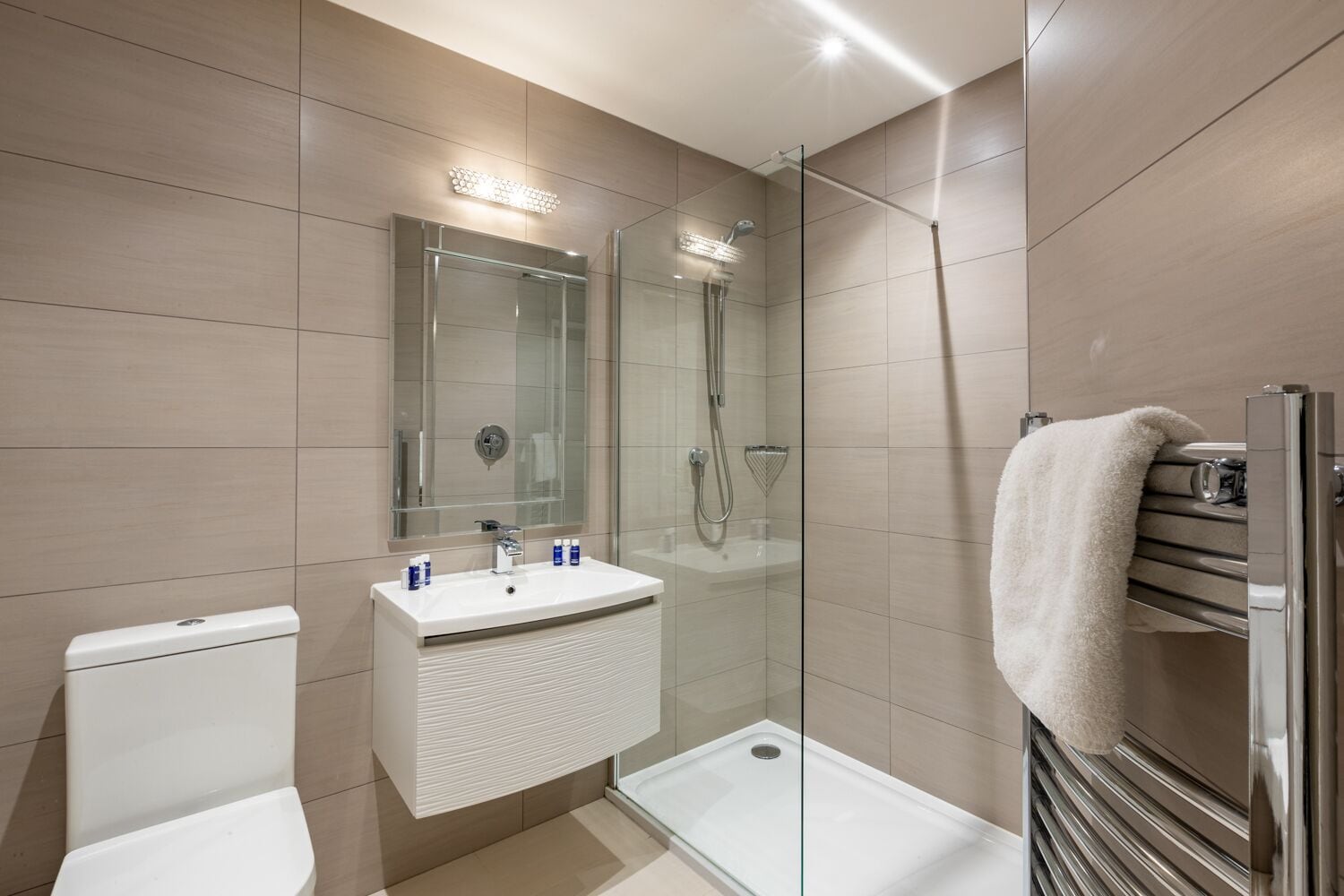 Une salle de bain moderne avec une douche à parois de verre, un lavabo blanc avec un miroir au-dessus, et un porte-serviettes sur lequel est posée une serviette blanche.