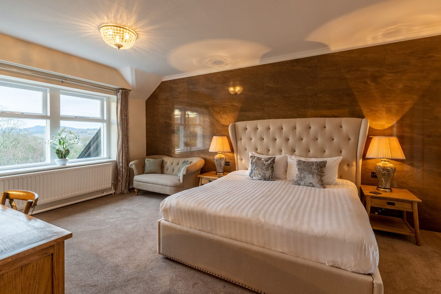 Een slaapkamer met een groot bed, een sofa, een bureau en uitzicht op het groen.
